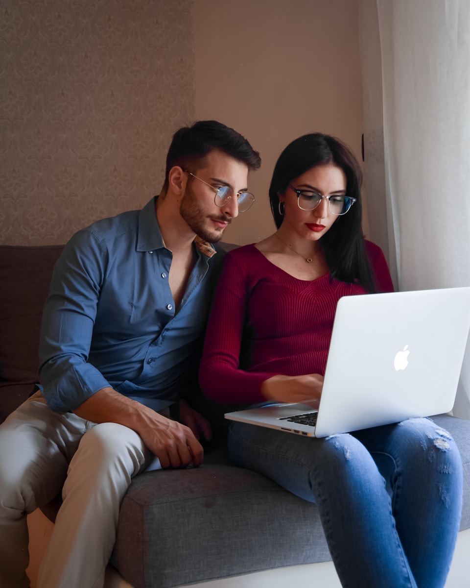 A man and woman sitting on a couch looking at a laptop